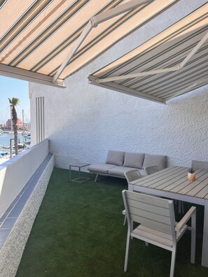 A balcony with a green artificial turf, a white sofa, a wooden table, and a metal chair. - Appart.90 m² -Exceptional Sea View-Renovated 2025 8-pers.- Large Terrace, Garage (Le Barcarès)
