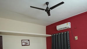 Ein Schlafzimmer mit Bett, Deckenventilator, Klimaanlage und einer roten Wand.
