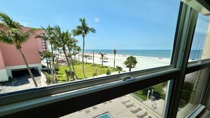 Blick aus einem Fenster auf Pool, Strand und ein Hotelgebäude.