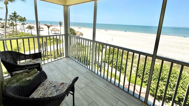 Ein Balkon mit Korbmöbeln, Blick auf einen Strand und einem klaren Himmel.