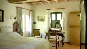 Een slaapkamer met een bed, een bureau, een stoel, een raam met gordijnen, een radiator en een deur.