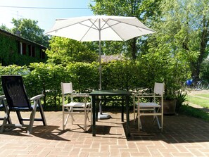 Un patio al aire libre con una mesa, sillas, un paraguas grande y una planta en maceta.