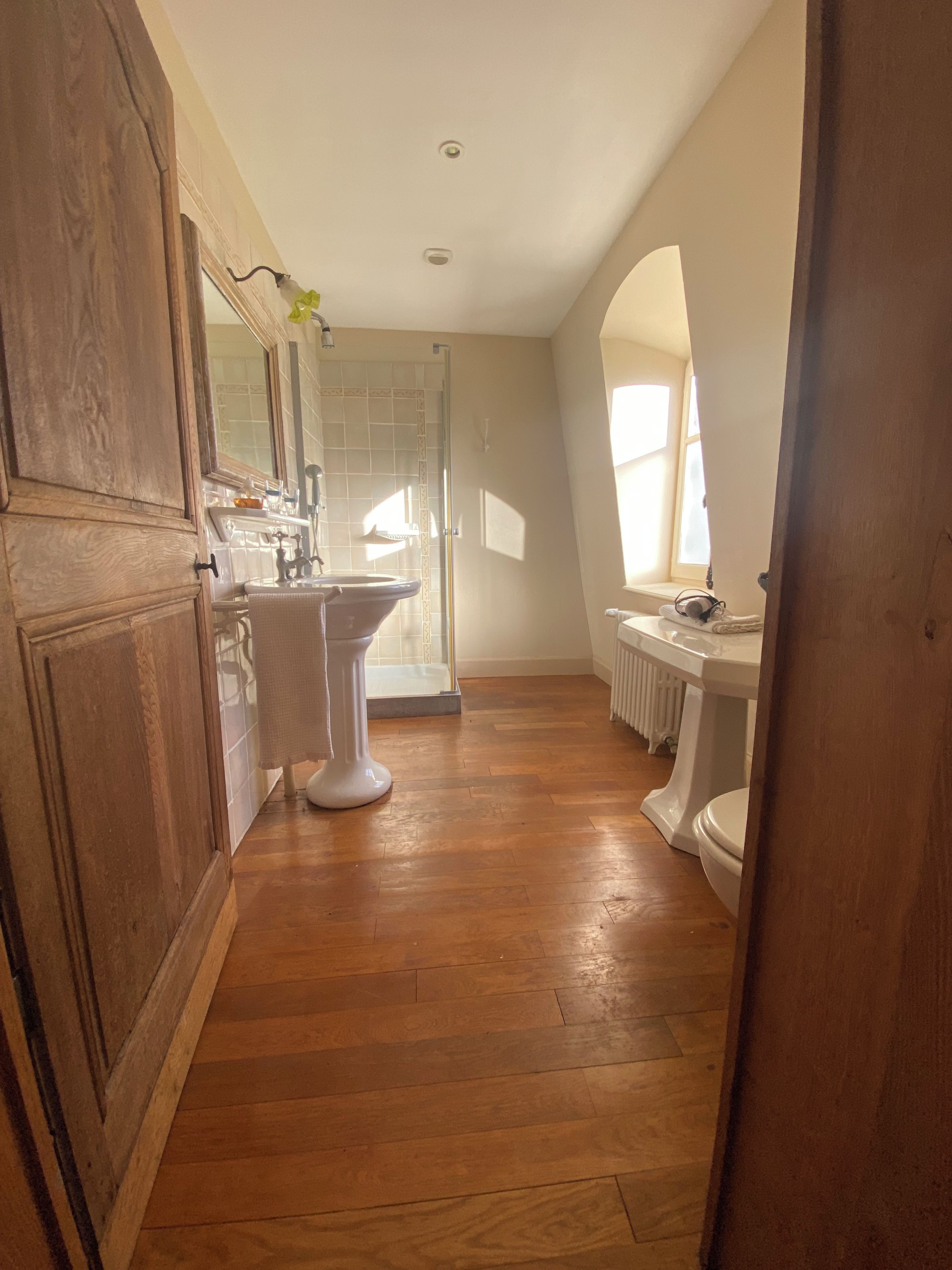 Een badkamer met een houten vloer, een wastafel op voet, een toilet en een douchegedeelte.