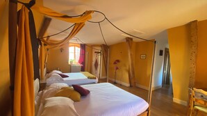 A room with two beds, a wooden floor, a chair, and a window with curtains.