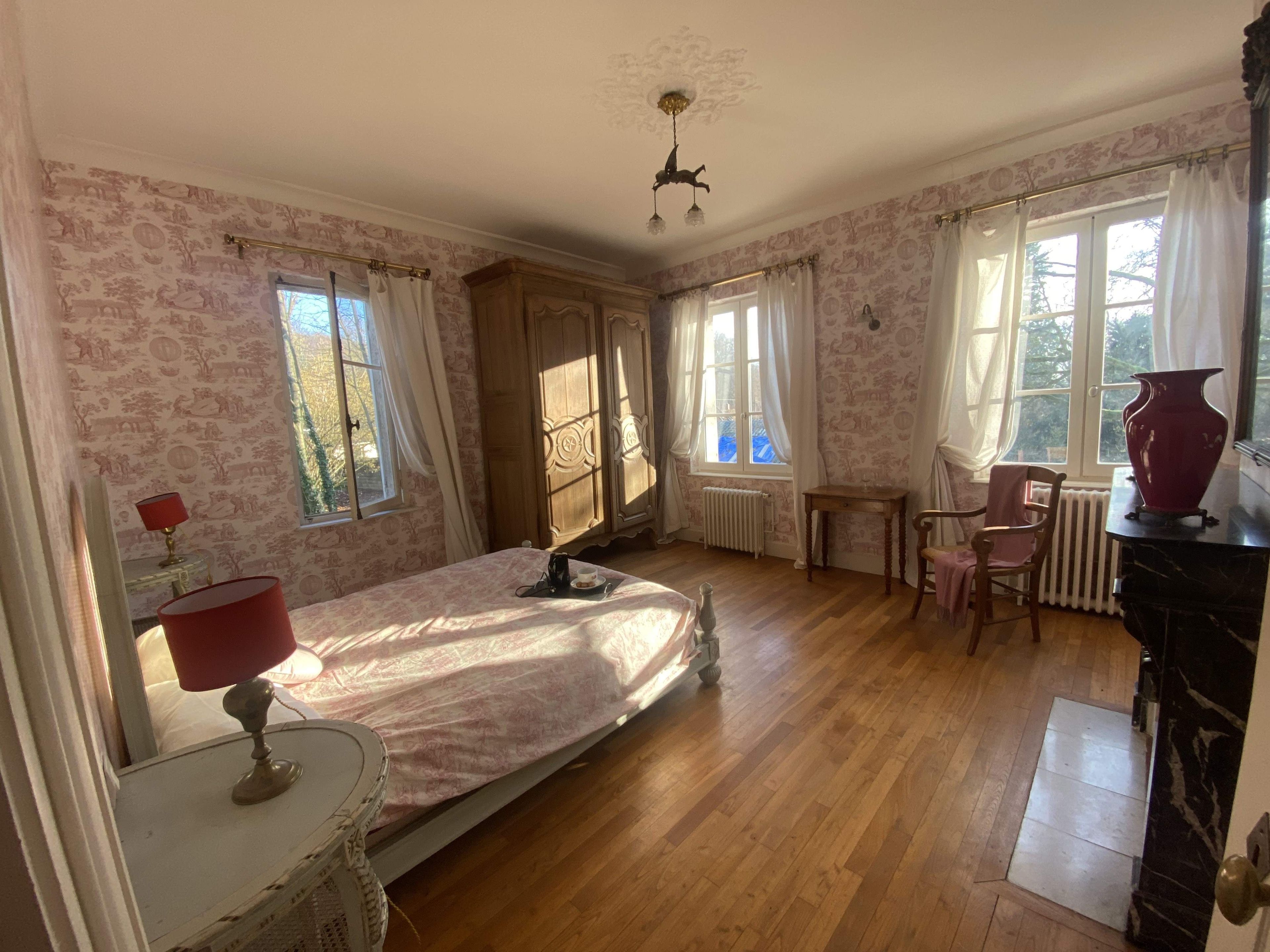 A bedroom with a bed, a chair, a table, a radiator, and a window with curtains.