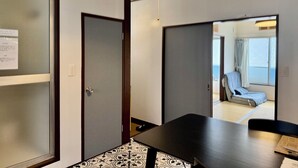 Ein Hotelzimmer mit einem großen Bett, einem Schreibtisch und einem Stuhl. Es gibt ein Fenster mit Vorhängen sowie eine Tür mit einem Hinweisschild.