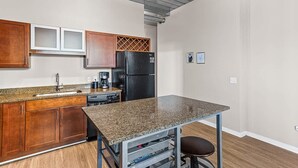 A compact kitchen with wooden cabinets, a granite countertop, a black refrigerator, and a coffee maker.