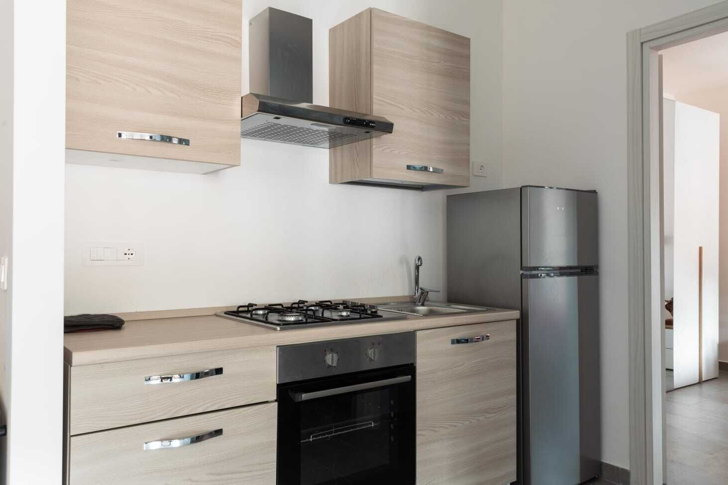 A modern kitchen with a gas stove, oven, stainless steel refrigerator, and wooden cabinetry.