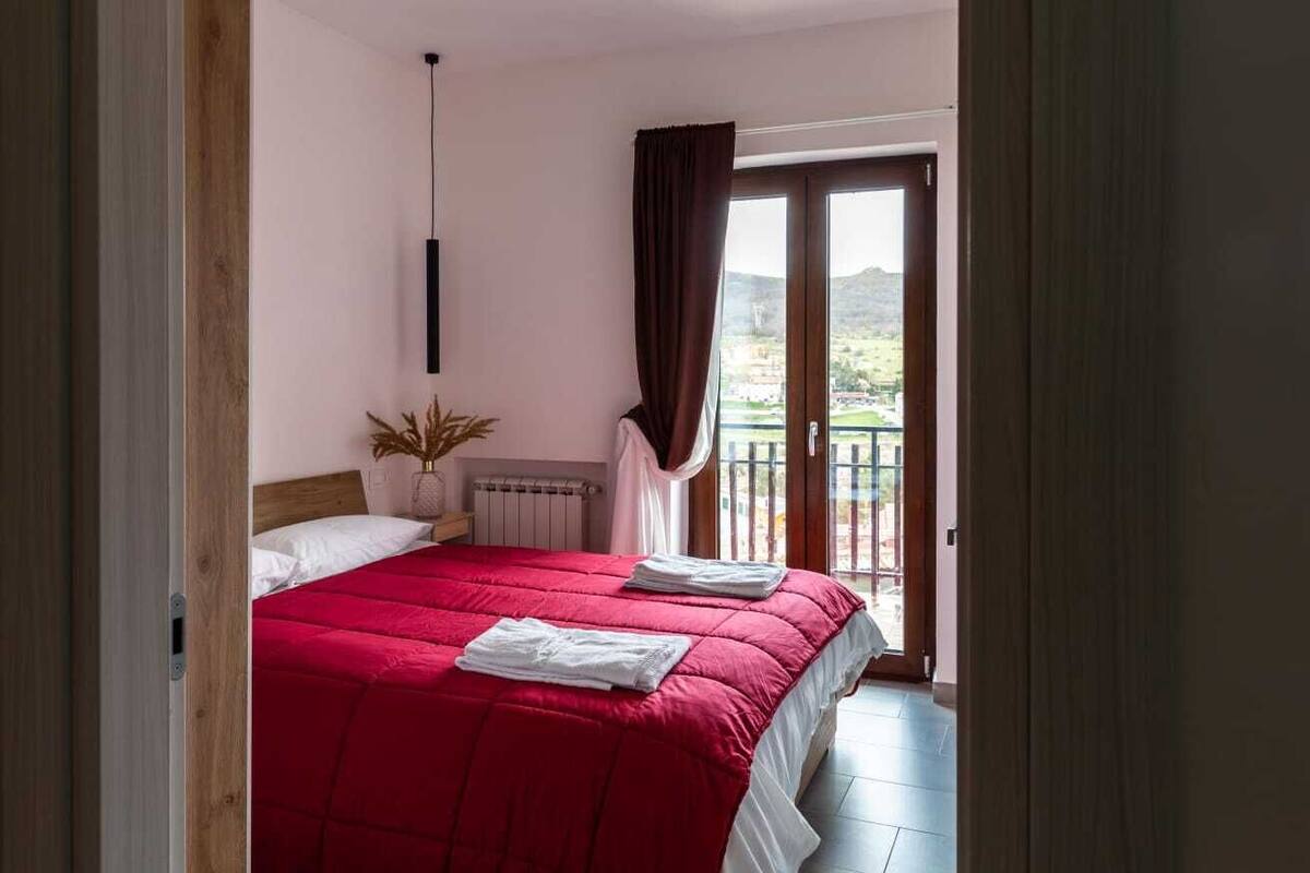 Una camera da letto con una coperta rossa, una pianta in vaso e vista su un balcone con una porta.