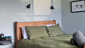 A bed with a wooden headboard, green bedding, and a gray pillow. There are wall-mounted light fixtures and a framed picture on the wall. - Greenvale Bed and Breakfast (Oban)