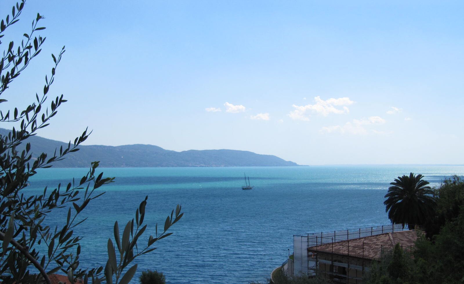 Vista sulla costa con cielo sereno, mare calmo e montagne in lontananza.