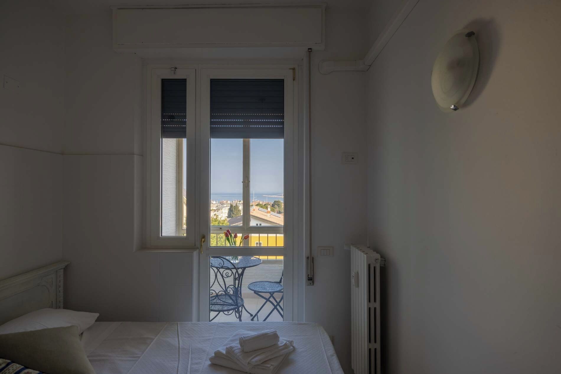 Un dormitorio con cama, ventana con vista a la ciudad y balcón con mesa y sillas.