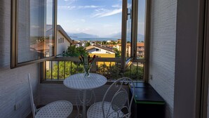 A balcony with a table and chairs, a vase with flowers, and a view of a coastal town. - Exclusive apartment a stone's throw from the station spectacular lake view Daisy  (Desenzano del Garda)