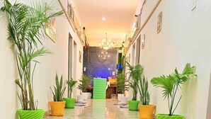 Un pasillo con plantas en macetas, un candelabro y una habitación iluminada en azul al fondo.