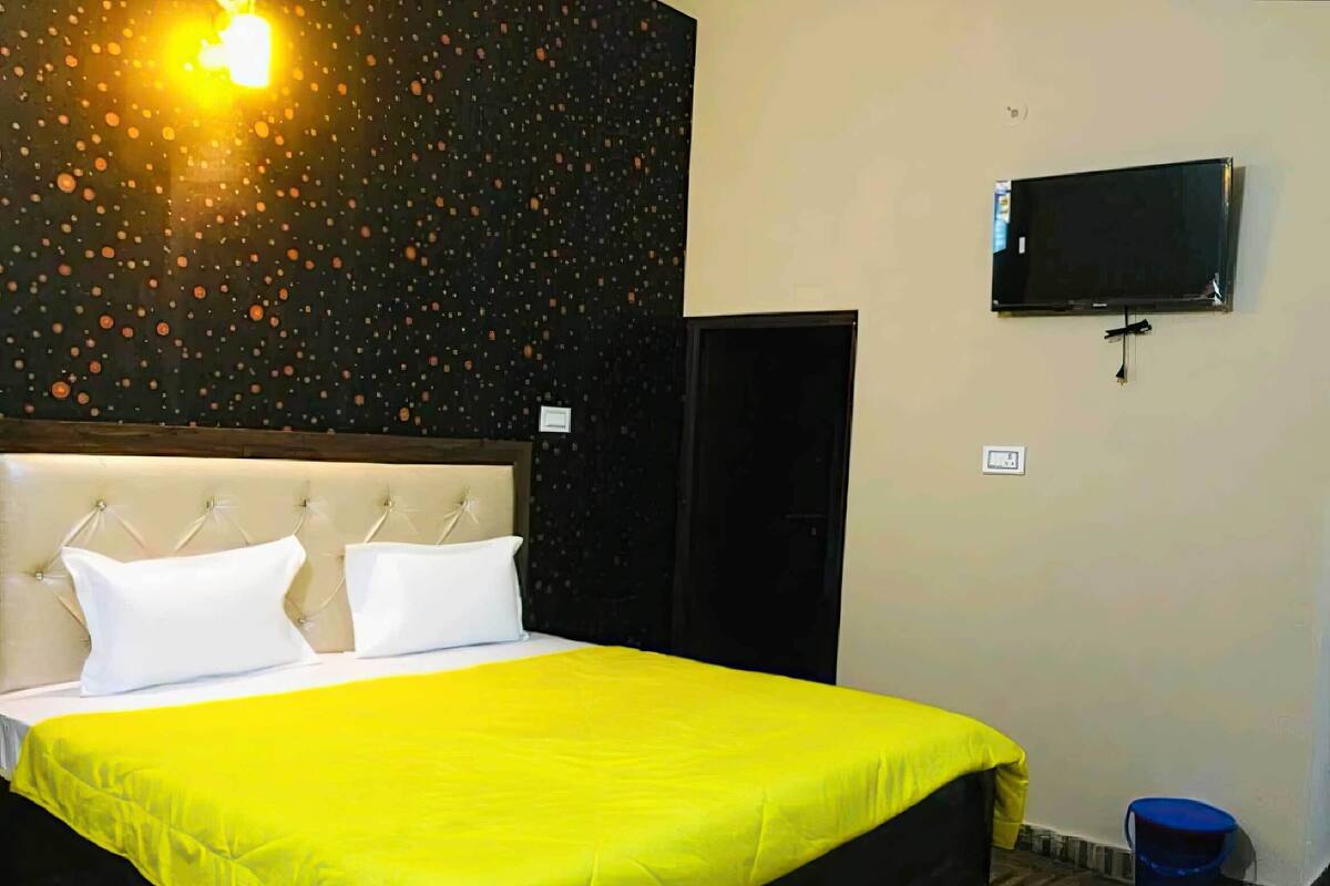 A hotel room with a bed, a TV, a door, and a bucket.