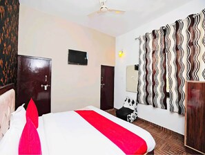 A hotel room with a bed, a wardrobe, a television, a mirror, and a patterned curtain.