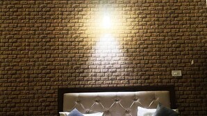 Una cama con cabecera capitonada, dos almohadas y una pared con diseño de ladrillo con una fuente de luz arriba.