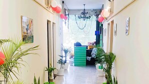 Un pasillo con plantas en macetas a ambos lados, un mostrador verde al final y un ventilador de techo.