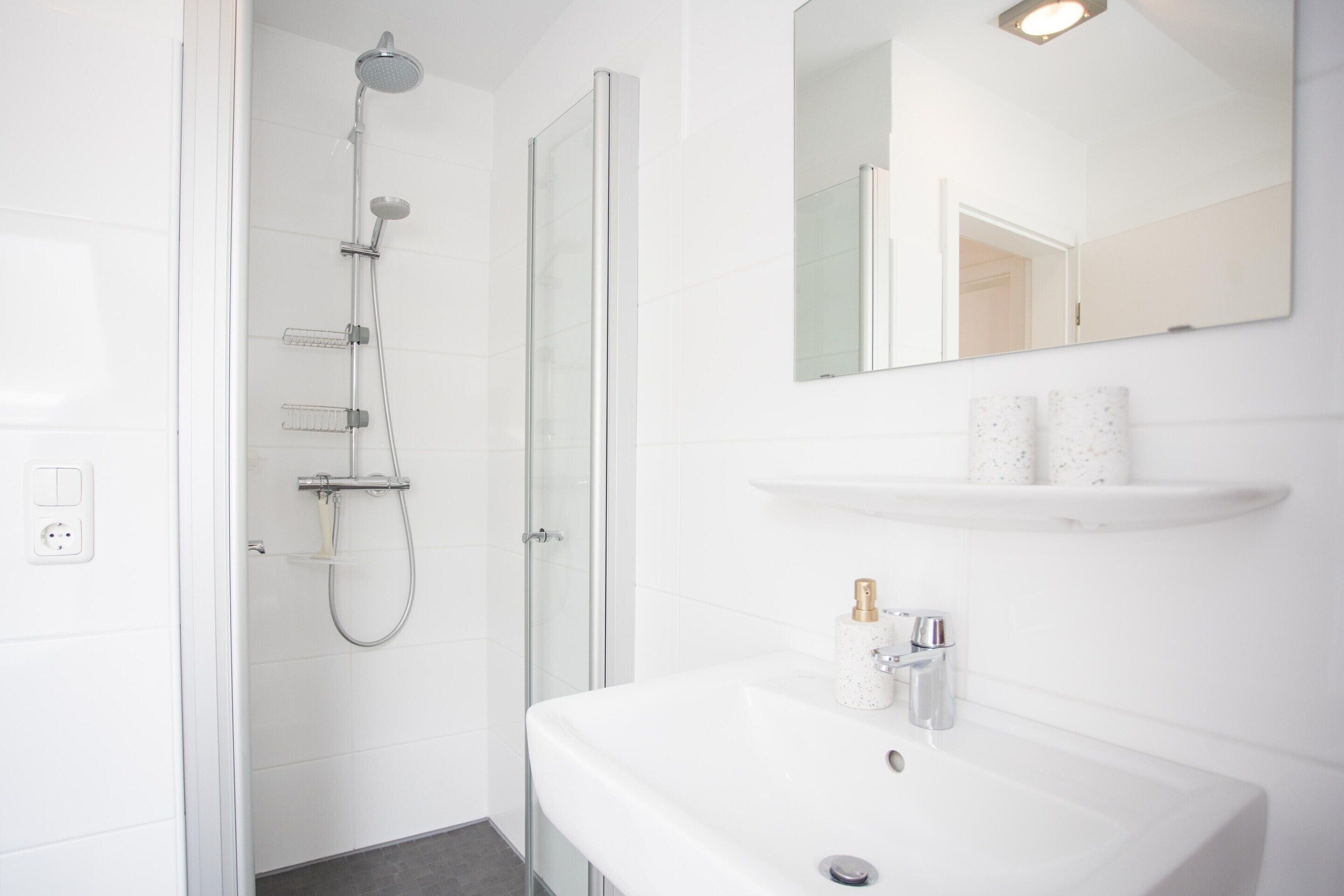 A modern bathroom with a glass-enclosed shower, a white sink, and a mirror above it.