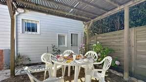 A covered patio with a table set for a meal, surrounded by white plastic chairs. - Brin de Muguet by Interhome (Tharon Plage)