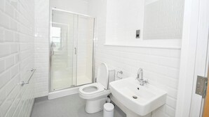 A bathroom with white tiled walls, a glass shower enclosure, a white toilet, and a sink with a mirror above it.