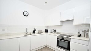 A modern kitchen with white cabinets, a stainless steel oven, a microwave, a coffee maker, and a clock on the wall.