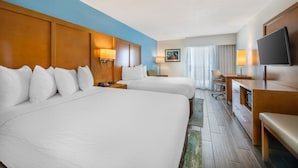 Habitación de hotel con dos camas, un escritorio, un televisor y una ventana con cortinas.