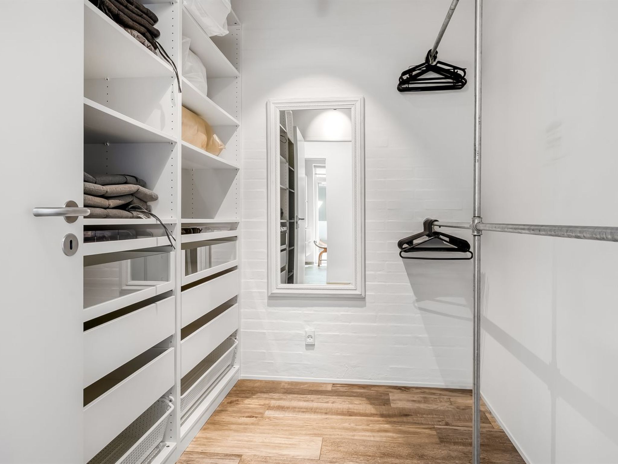 Un dressing accessible sans porte, doté d’étagères ouvertes, d’une tringle à vêtements et d’une porte donnant sur une autre pièce.