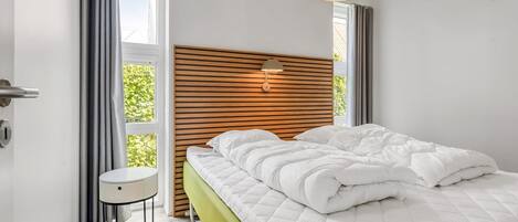 A modern bedroom with a wooden headboard, a bedside table, a green bedspread, and a hanging light fixture.
