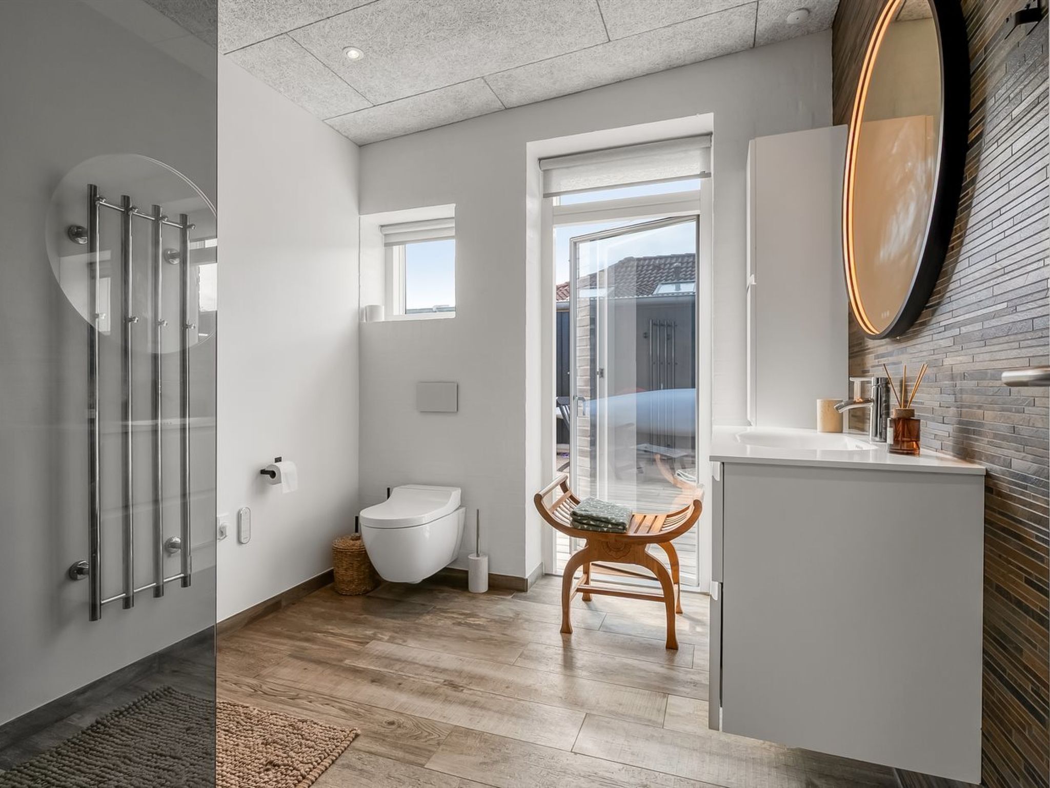 A modern bathroom with a glass shower enclosure, a toilet, and a wooden chair.