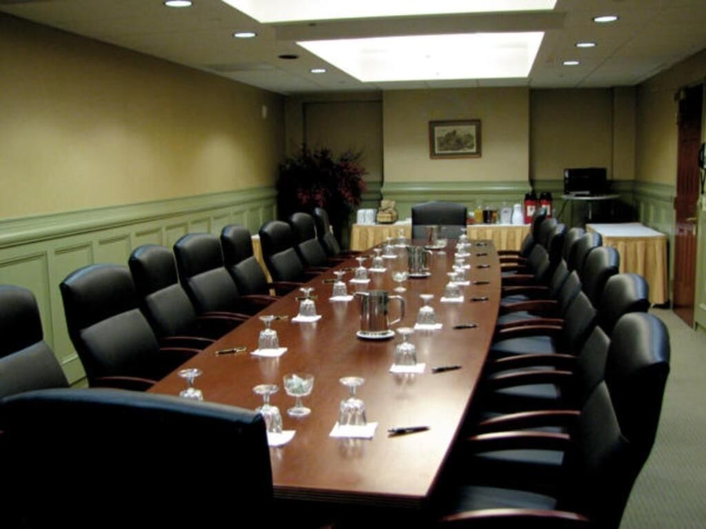 Une salle de conférence avec une longue table, des chaises noires et une plante en arrière-plan.