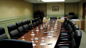 Une salle de conférence avec une longue table, des chaises noires et une plante en arrière-plan.