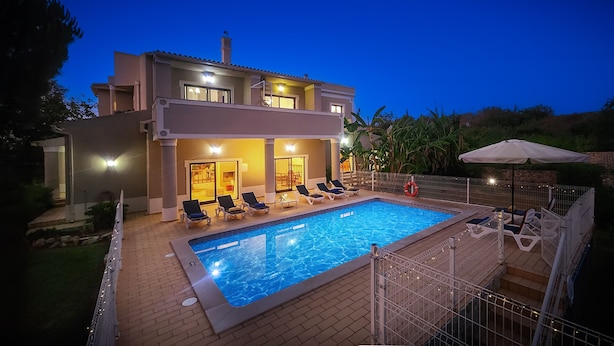 A modern two-story house with a swimming pool, outdoor seating, and a well-lit patio area.