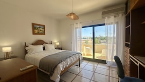 A hotel room with a bed, bedside lamps, a desk, a chair, and a balcony with a view.