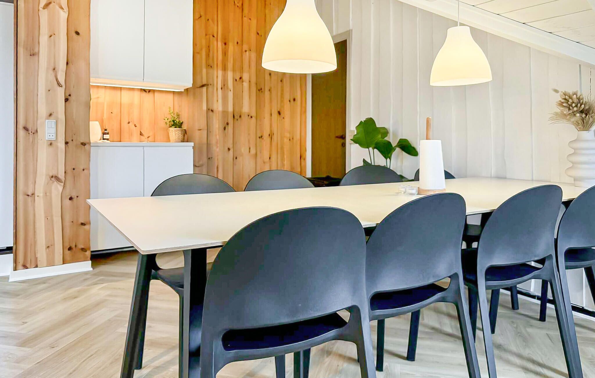 Un espace repas moderne avec une longue table, six chaises et des luminaires suspendus.