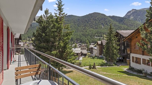 A balcony with a view of a mountain village, wooden buildings, and a grassy area. - Zermatt, 4 pers/3 lits - Balcon avec vue & jardin (Zermatt)