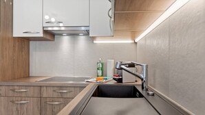 A modern kitchen with wooden cabinets, a stainless steel sink, and a built-in range hood. - Zermatt, 4 pers/3 lits - Balcon avec vue & jardin (Zermatt)