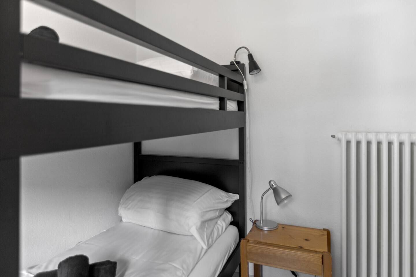 A bunk bed with a bedside table and lamp, a radiator, and a wooden nightstand.