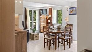 A dining area with a wooden table and chairs, a television mounted above the table, and a window with curtains. - Zermatt, 4 pers/3 lits - Balcon avec vue & jardin (Zermatt)