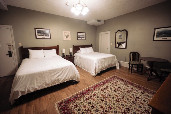 Une chambre d’hôtel avec deux lits, un plancher en bois, un tapis à motifs, une table à manger et un miroir au mur.