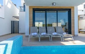 A modern outdoor pool area with four lounge chairs and a glass door entrance. - Pet friendly home in San Javier (San Javier)