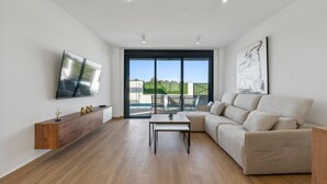 Ein modernes Wohnzimmer mit Sofa, Couchtisch, Fernseher und großem Fenster mit Blick auf einen Swimmingpool.