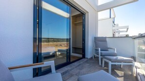 Ein Balkon mit Glastür, die zu einem Innenraum führt, ein weißer Stuhl und ein zweiter Stuhl mit Sitzkissen.