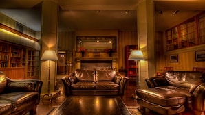 A cozy living room with leather sofas, a fireplace, bookshelves, and lamps.