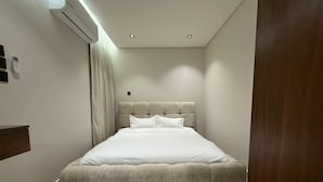 A bedroom with a bed, an air conditioning unit, a bedside table, and a wooden door. - Luxury & Comfort in Prime Al-Qairawan Location!
Modern Design, 5G Internet (Riyadh)