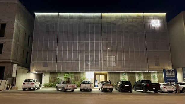 A modern building with a large glass facade and a Nissan car parked in front. - Luxury & Comfort in Prime Al-Qairawan Location!
Modern Design, 5G Internet (Riyadh)