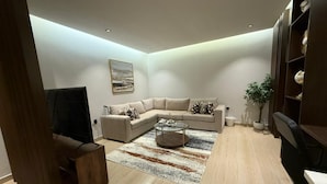 A modern living room with a beige sectional sofa, a coffee table, and a TV. There is a wooden cabinet and a potted plant. - Luxury & Comfort in Prime Al-Qairawan Location!
Modern Design, 5G Internet (Riyadh)