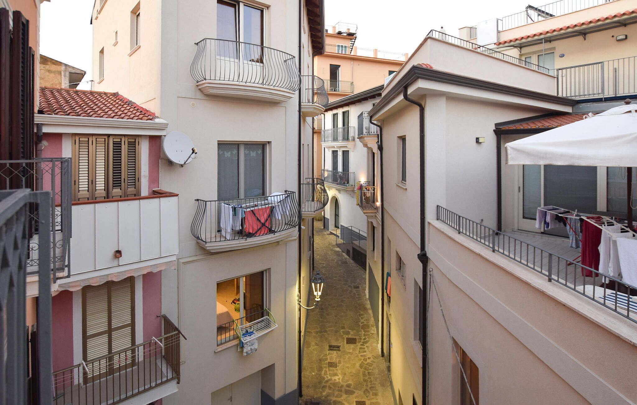 A narrow alleyway between buildings with balconies, some with clothes drying.