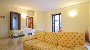 Ein Wohnzimmer mit gelber, gemusterter Couch, einem Esstisch mit Stühlen und einem Fenster mit Blick.