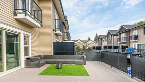 Een modern appartementencomplex met een patio, voorzien van een grijze modulaire bank, kunstgras en een bolvormige lamp.